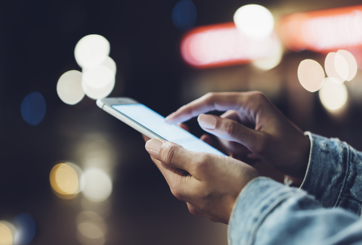 Girl pointing finger on screen smartphone on background illumination bokeh color light in night atmospheric city, hipster using in female hands and texting mobile phone, mockup glitter street, content lifestyle