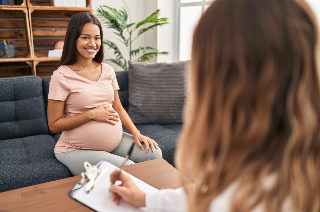 Young pregnant woman at therapy session looking positive and happy standing and smiling with a confident smile showing teeth